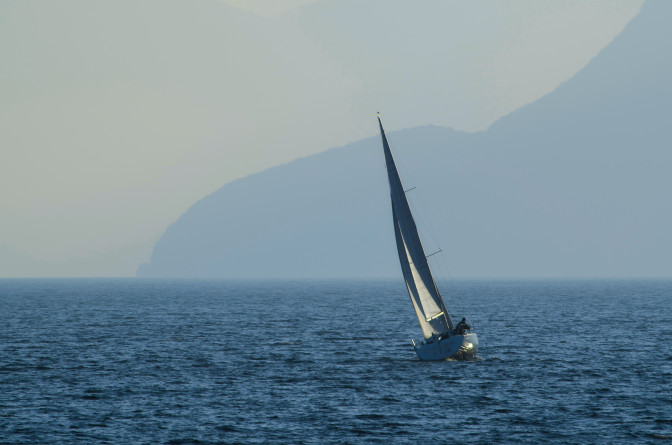 small-sailing-ship-sea-surrounded-by-mountains-covered-fog-daytime.jpg