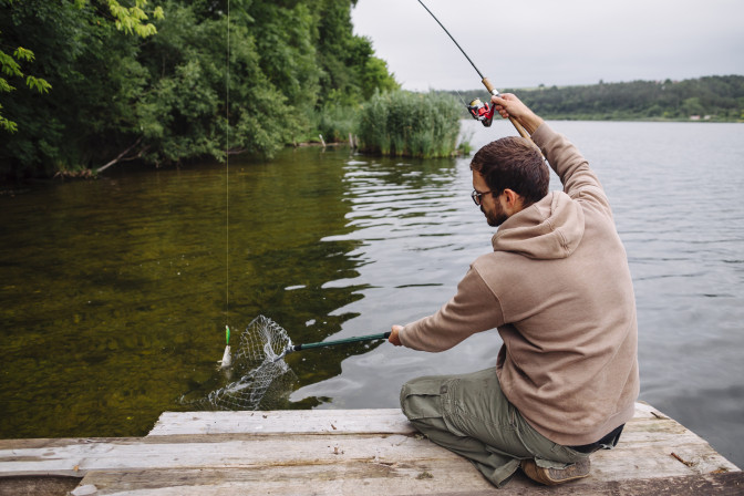 man-sitting-pier-catching-fish-with-fishing-rod.jpg